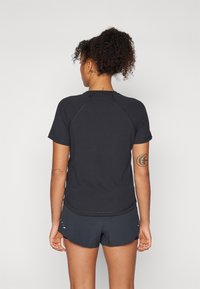 Svart sports t-skjorte med korte raglan-ermer, glatt stoff, buet bunn, kombinert med matchende mørke shortser. Synlige arm-tatoveringer.