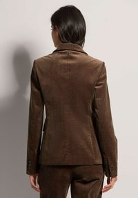 Brauner Cordblazer mit vertikaler Ripptextur, schmalem Revers und geknöpften Manschetten. Taillierte Passform, Rückenschlitz und strukturierte Silhouette.