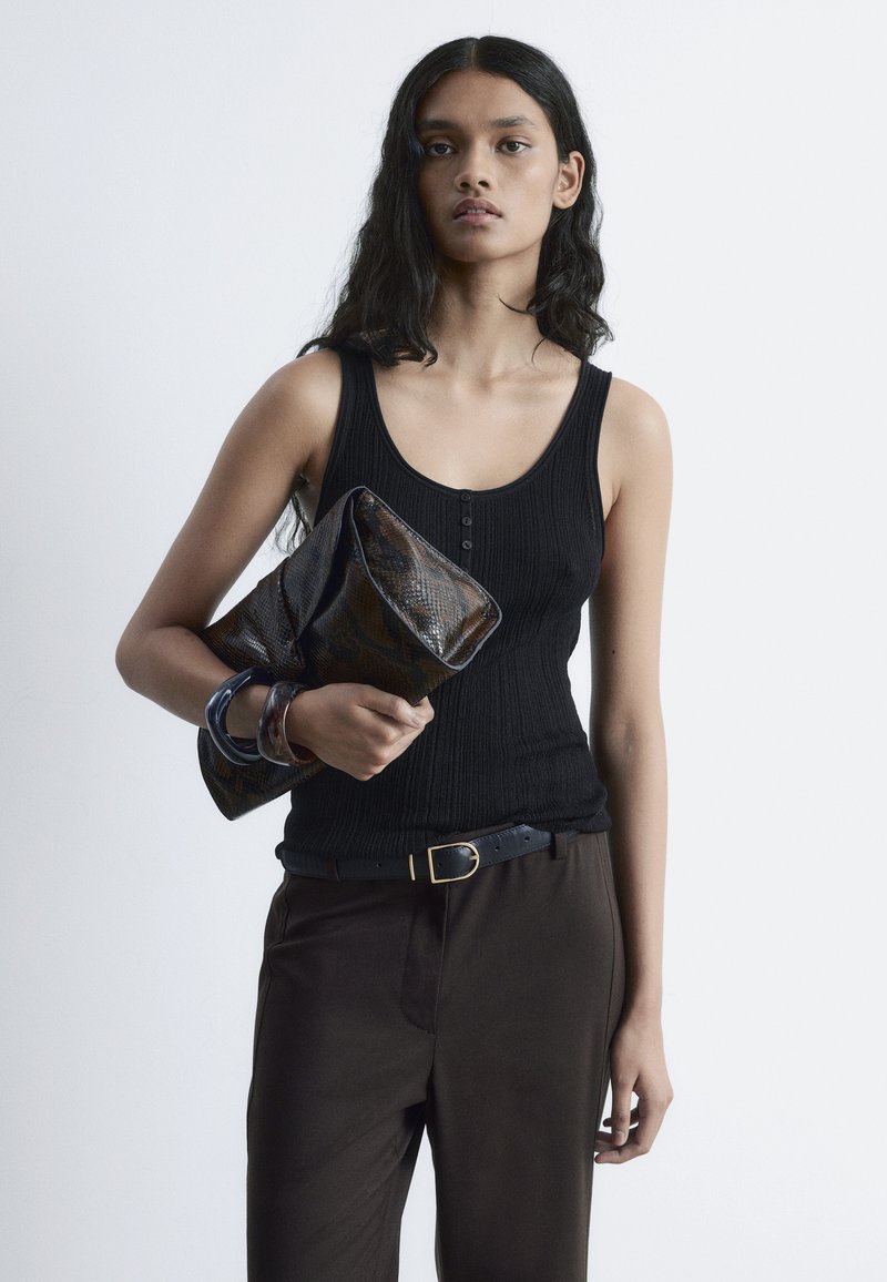 Black ribbed tank top with a scoop neckline, brown high-waisted pants, a dark patterned clutch, and a black belt with a gold buckle detail.