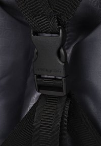 Gros plan d'une boucle en plastique noir avec des sangles tissées attachées à l'intérieur d'une doublure en tissu gris foncé.
