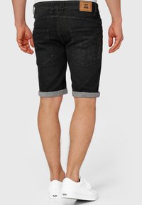 Pantaloni scurți din denim negru cu tivuri întoarse. Prezintă o etichetă din piele maro pe banda de sus din spate și două buzunare posterioare. Purtați cu adidași albi.