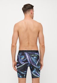 Boxer-briefs pour hommes avec une ceinture noire portant le logo "UNUR". Le tissu présente un motif de peau de serpent coloré dans des tons de bleu et de vert.