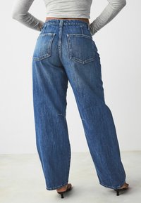 Jeans in denim blu a gamba larga con vita alta, design a cinque tasche e leggero sbiadimento; presentano un taglio dritto fino alla caviglia.