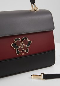 Sac à main en cuir avec des panneaux noirs, bordeaux et gris, doté d'un fermoir fleur doré et noir et d'une bandoulière noire amovible avec des accessoires dorés.
