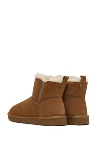 Braune Wildlederstiefeletten mit einem weichen, cremefarbenen Kunstfellfutter, runder Zehenform und flacher Gummisohle. Mit einer kurzen Zuglasche an der Rückseite.