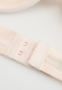 Beżowy pasek od stanika z podwójnym zapięciem na haftekę oraz elementem z siateczki na jednolitej białej powierzchni.