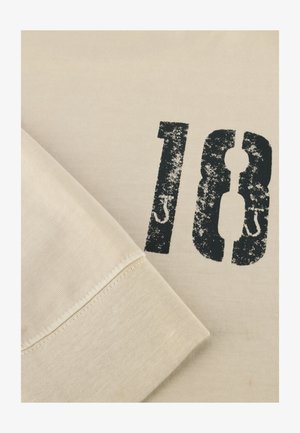 Cremfarbener T-Shirt mit einem abgenutzten schwarzen "18" Druck. Weicher, strukturierter Baumwollstoff mit Rundhalsausschnitt und genähten Ärmelabschlüssen.