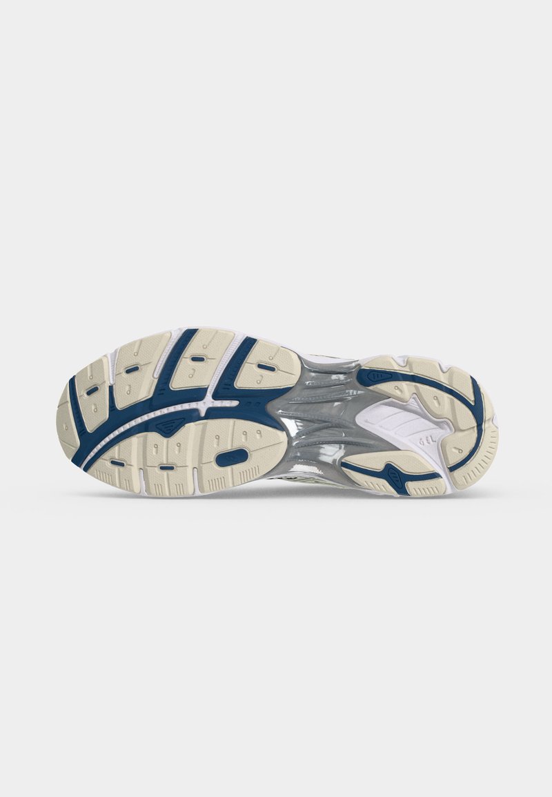 Suela de zapatilla con banda de rodadura de goma beige y azul marino, soporte de entresuela gris, mostrado sobre un fondo liso gris claro.