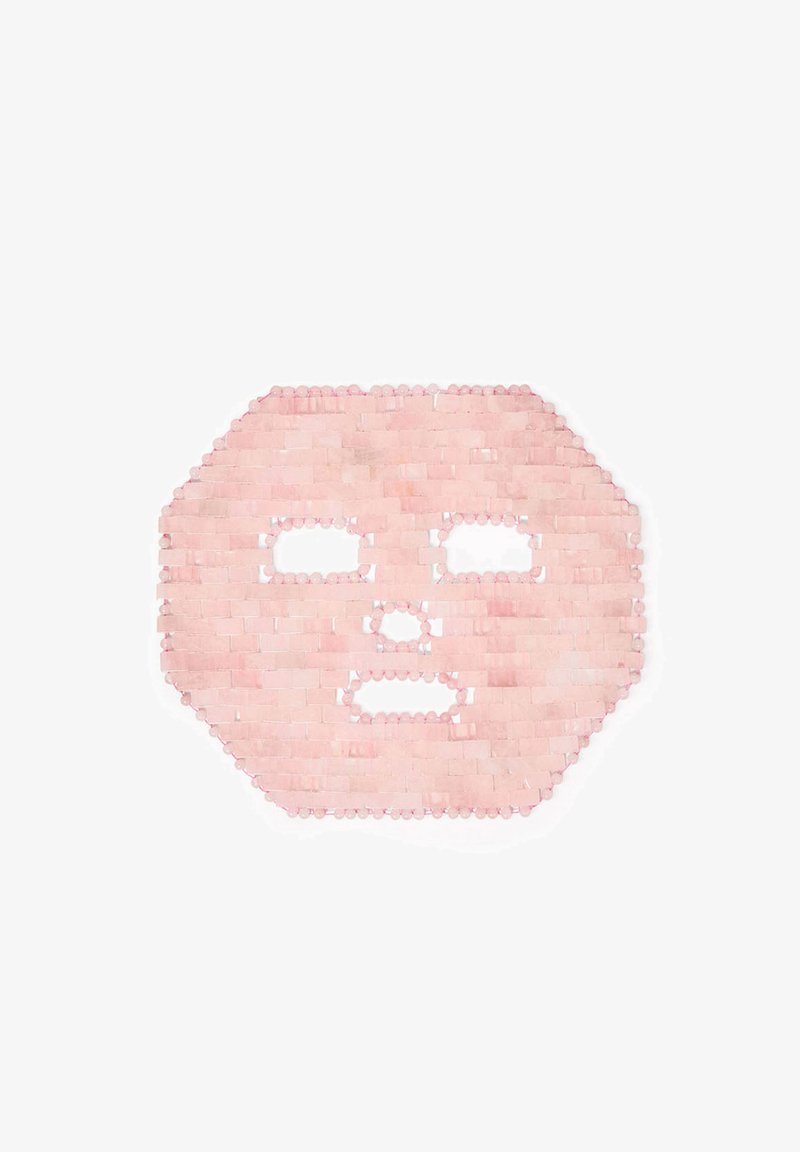 Masque facial tissé rose avec des ouvertures ovales pour les yeux et la bouche, possédant une surface texturée et des bords faits de perles petites et alternées.