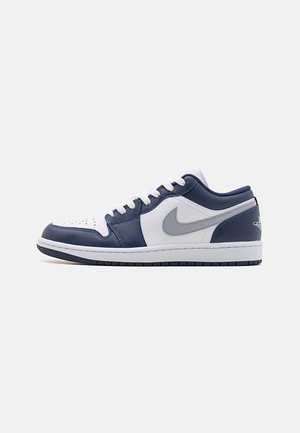 Nízké tenisky s vrchní částí z bílého, námořnického a šedého kůže. Obsahují perforovanou část pro prsty, bílé tkaničky a šedé logo Nike po straně.