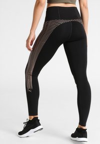 Leggings atletici neri con vita alta, dotati di un motivo geometrico in rete color rosè dorato sui lati. Realizzati in tessuto elastico.