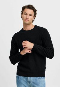 Zwarte lange mouwen trui met een geribbelde textuur, ronde hals en raglanmouwen, gedragen over lichtblauwe jeans. Eenvoudig en klassiek ontwerp.