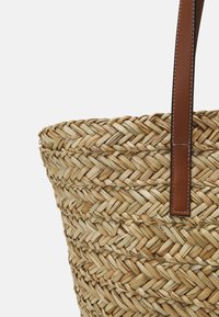 Sac en paille tressée de forme ronde, doté d'une anse en cuir beige et de détails de couture visibles. Des tons beiges naturels dominent le design.