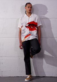 Chemise blanche à manches courtes avec un graphique de lèvres rouges, assortie à un pantalon noir et des baskets beiges. Présente un fit décontracté et un tissu brillant.