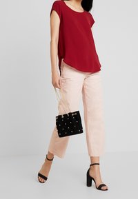 Czerwony top z krótkim rękawem, luźny fason, zestawiony z jasnoróżowymi szerokimi spodniami. Akcesoria to czarna aksamitna torba typu bucket z złotymi detalami.