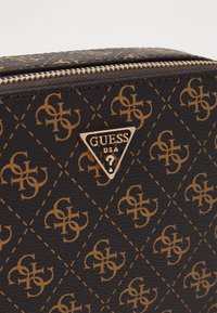 Borsa nera in ecopelle con triangolo logo dorato e motivo a logo ripetuto. Chiusura con zip e dettagli di cucitura.