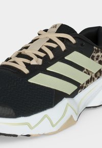 Μαύρο και μπεζ αθλητικό παπούτσι Adidas με υφή στη μύτη, μπεζ κορδόνια, τρεις ανοιχτό πράσινες ρίγες, πλευρικό πάνελ με λεοπάρ μοτίβο και λευκή σόλα.