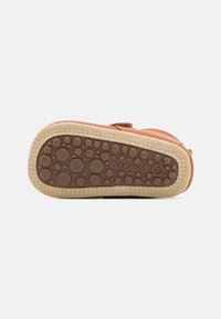 Zapato de cuero marrón con una suela de goma texturizada que presenta patrones circulares. Costuras visibles alrededor del borde y el nombre de la marca grabado.