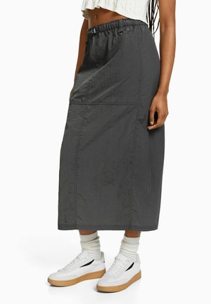 Mørkegrå midinederdel i taljen med elastisk taljebånd og sidelomme, båret med hvide sokker, hvide sneakers og cropped hvid top.