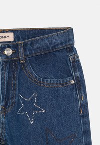 Jeans iz jeansa s temno modrim pranjem, srebrnimi dodatki in okrasnimi zvezdami, okrašenimi z rhinestones na sprednjem žepu.