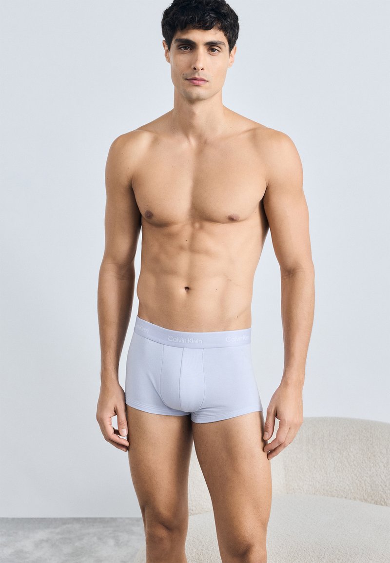 Boxeri scurți gri deschis dintr-o țesătură moale, cu un tiv neted etichetat "Calvin Klein". Design ajustat, material elastic.