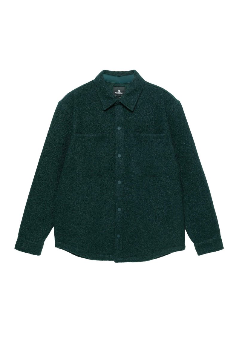 Giacca camicia in pile verde scuro con chiusura a bottoni, colletto a punta, due tasche sul petto e maniche lunghe. Texture morbida e design casual.