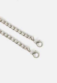Kjedet er laget av sølvfarget metall med store ledd, og har to krabbe-klips i hver ende. Det har en glatt, blank tekstur og en sømløs design.