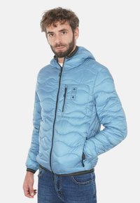 Giacca imbottita azzurro chiaro con motivo trapuntato ondulato, cappuccio, cerniera frontale e due tasche con cerniera. Tessuto morbido e liscio.