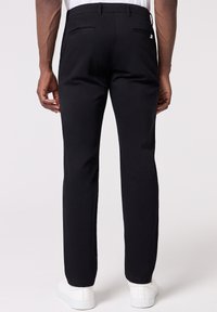 Pantaloni neri con taglio slim, caratterizzati da una texture liscia, due tasche posteriori e vita a media altezza, abbinati a sneakers bianche.