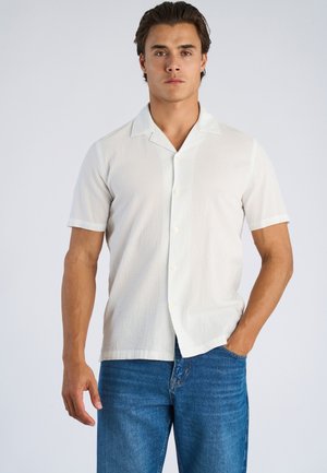 Biały, teksturowany T-shirt z krótkim rękawem i kołnierzykiem, z zapięciem na guziki z przodu i luźnym krojem, zestawiony z niebieskimi dżinsami.