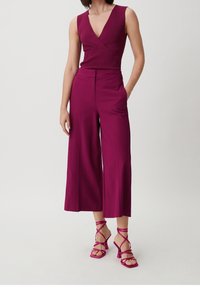 Top sans manches fuchsia avec une texture côtelée, assorti à un pantalon large fuchsia et des escarpins à talons carrés avec des lanières de la même couleur.