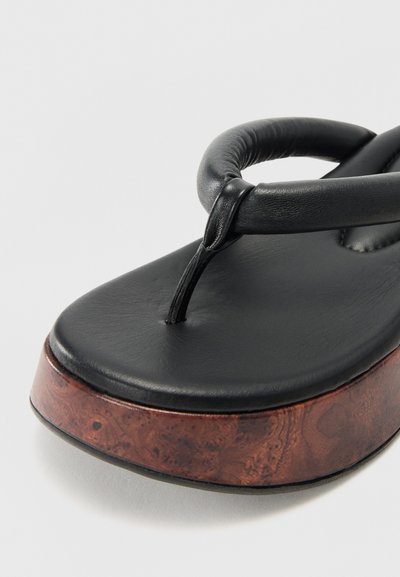 Černé kožené flip-flop sandály s texturovaným, polstrovaným svrškem a hnědou dřevitou platformou. Disponují jednoduchým designem s páskem mezi prsty.