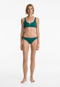 Zeleno modri bikinij set ribaste strukture, ki vključuje bralette zgornji del z V-oblikovanim izrezom in ustrezne nizke spodnjice. Gladka tekstura, minimalna oprema.