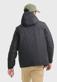 Schwarz-gesteppten Kapuzenjacke mit glatter, matter Oberfläche, verstellbarer Kapuze und elastischen Bündchen, kombiniert mit khakifarbenen Hosen.