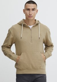Felpa beige con cappuccio, chiusura a metà con zip, tasca frontale e cordini. Materiale in cotone con una texture morbida e un sottile dettaglio del logo.