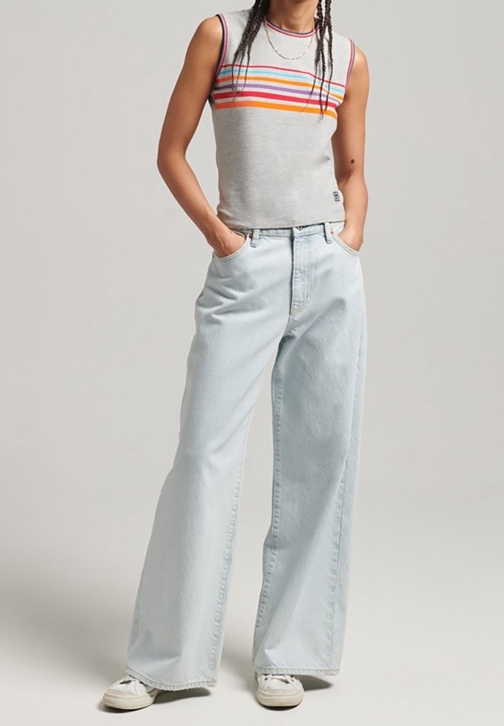 Šedý tílko bez rukávů s vícbarevnými vodorovnými pruhy v kombinaci s volnými světle modrými džínami a bílými teniskami.