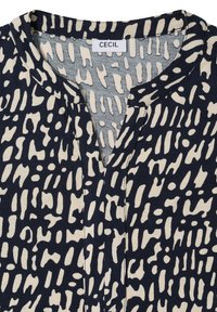 Marineblå og cremefarvet bluse med abstrakt, tekstureret mønster. Har en v-udskæring og en label med påskriften "CECIL" ved kraven. Blødt stof.
