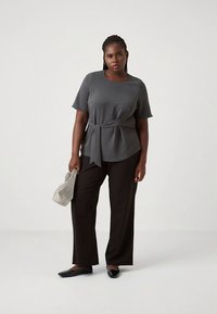 Grå blus med korta ärmar och knytning i midjan, kombinerad med svarta byxor med vida ben. Outfiten har en texturerad yta och en strukturerad silhuett.