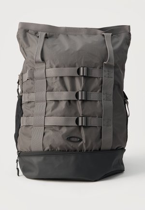 Zaino tattico grigio con tre cinghie orizzontali con fibbie e tasca inferiore nera, in piedi su uno sfondo bianco semplice.