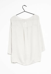 Leichte, langärmelige Bluse aus weichem, cremefarbenem Stoff mit rundem Ausschnitt, Rückenschlitzdetail und abgerundetem Saum, auf einem Kleiderbügel präsentiert.