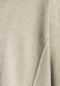 Beige svetr s měkkým, texturovaným pletením a žebrovanými detaily podél švů. Tkanina vypadá teple a útulně, ideální pro vrstvení.