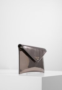 Pochette argentée métallique en forme d'enveloppe, finition brillante, avec un accent de marque. Présente un design épuré et minimaliste.