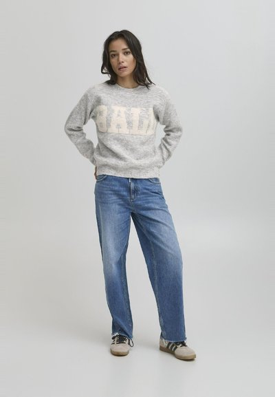 Lys grå strikket genser med "BALI" i kremfarge, sammen med løse blå denimjeans. Antrekket har casual joggesko med striper.