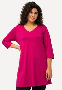 Fuchsia lange mouw tuniek met een V-hals, gemaakt van zachte stof. Heeft een losse pasvorm en een gebogen zoom, gecombineerd met zwarte leggings.