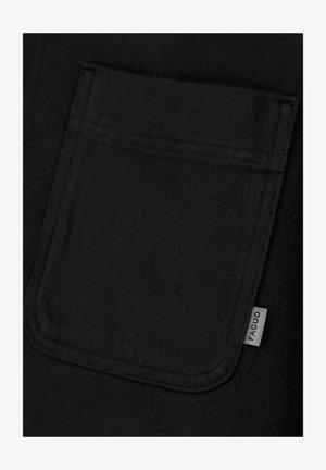 Nahaufnahme eines schwarzen Stoffes, der eine genähte Tasche zeigt, an der rechten Seite mit einem weißen Etikett mit der Aufschrift "FAGUO".