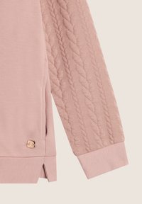 Maglietta a maniche lunghe rosa con un motivo a trecce testurizzato sulle maniche, fessure laterali e un piccolo logo metallico sul bordo.