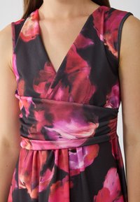 Robe à imprimé floral dans des couleurs sombres, présentant un décolleté en V, une taille cintrée et une jupe fluide. Accentuée par des teintes de rose et de rouge. Texture de tissu douce.