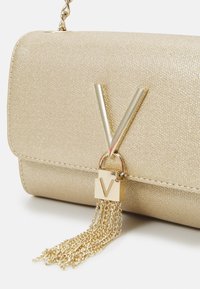 Borsa a tracolla metallica dorata con finitura testurizzata, caratterizzata da un grande hardware a forma di lettera "V" dorata e un dettaglio con frangia a catena dorata.