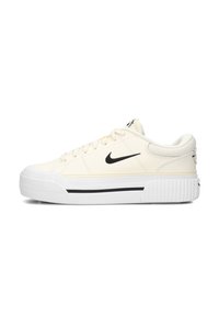 Zapatilla color crema con acentos negros, que presenta un upper de lienzo texturizado, puntera redonda, suela blanca gruesa y un destacado detalle de rayas.