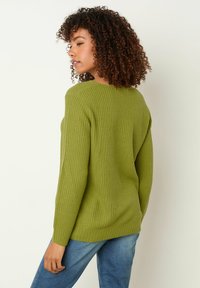 Grüner Rippstrickpullover mit langen Ärmeln, Rundhalsausschnitt und strukturierter Oberfläche. Über hellblauen Jeans getragen, mit einem entspannten Sitz und Fall.